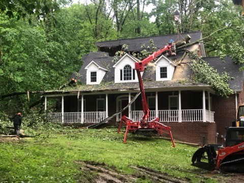 Crane lifting a fallen tree off a home after a storm